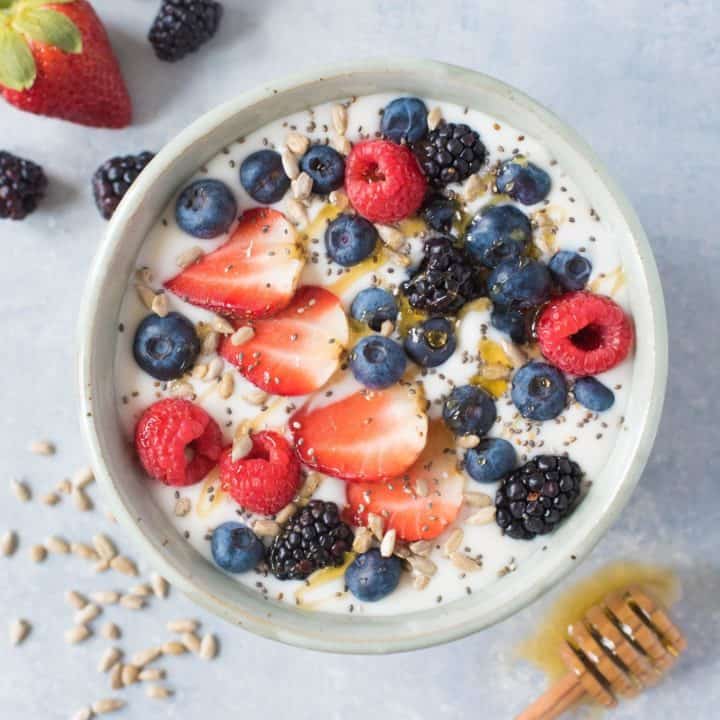 Overhead shot of Instant Pot coconut yogurt in a white bowl, garnished with mixed berries and seeds, and a drizzle of honey