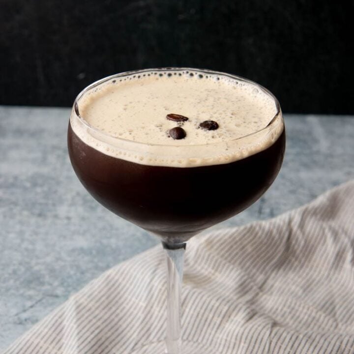 A coffee cocktail served in a coupe glass on a grey counter with a dark background.