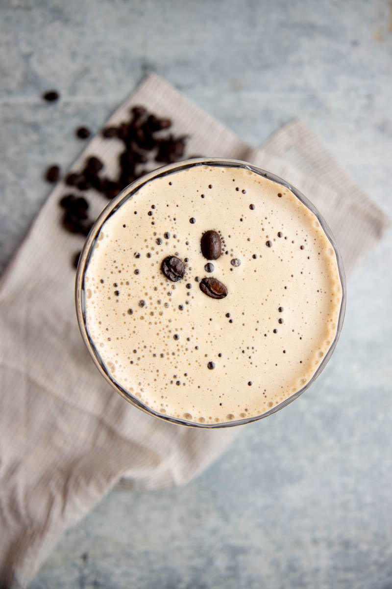 Top view of a coffee cocktail with a creamy foam and three espresso beans as garnish.