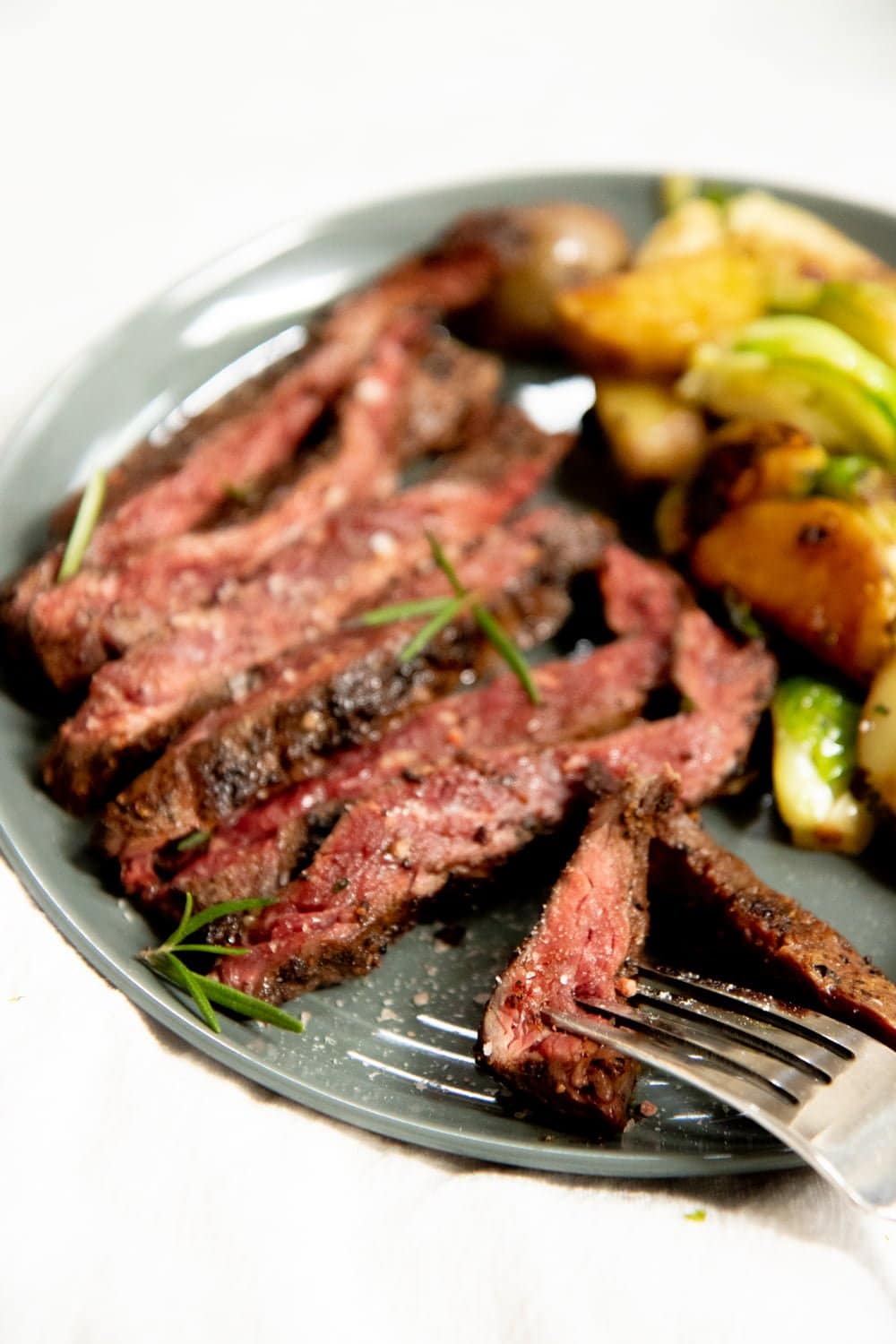 Seared steak on a grey plate, with potatoes and Brussels sprouts in the background