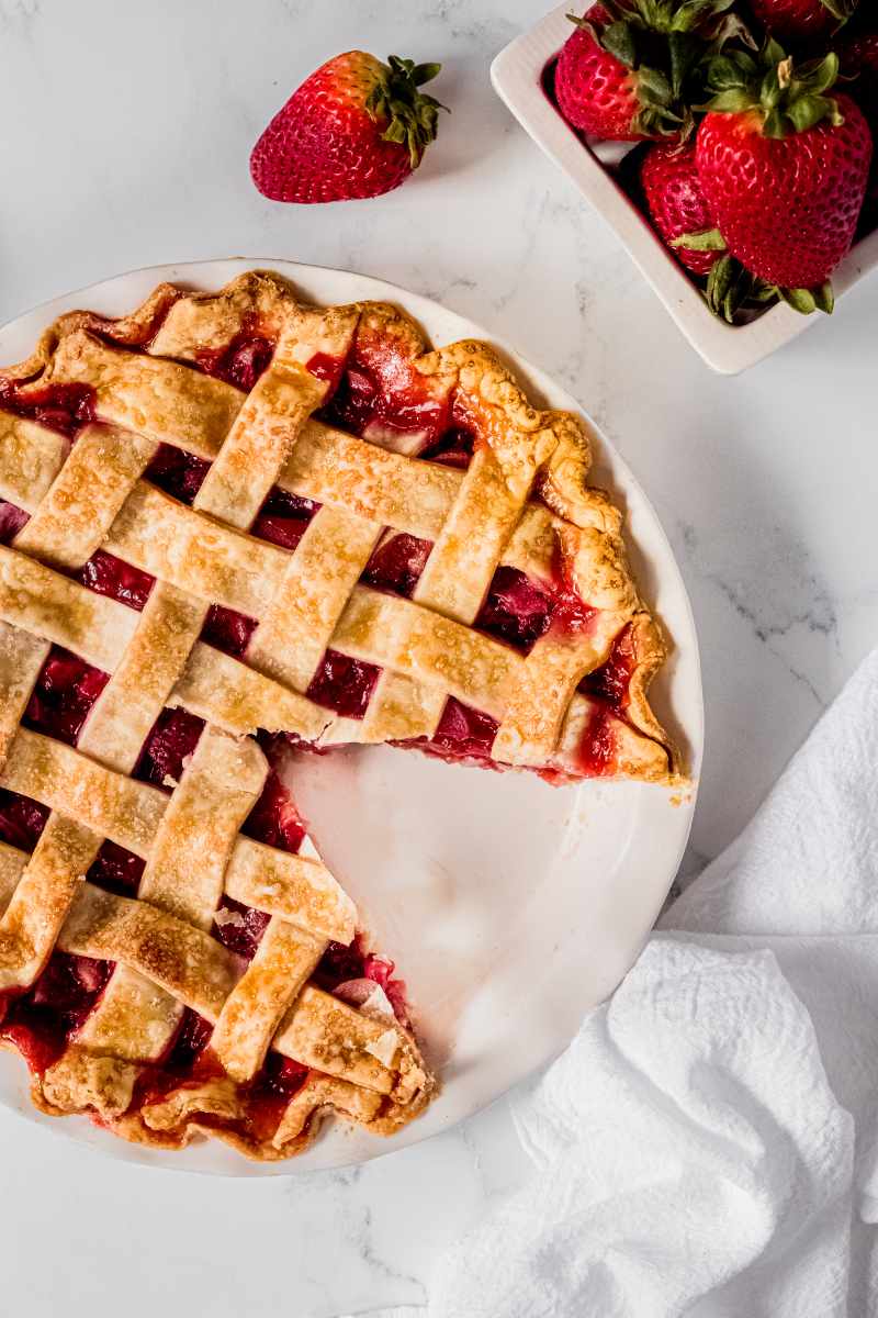 Overhead of cooled pie on the counter with one slice removed and fresh ripe strawberries beside it.