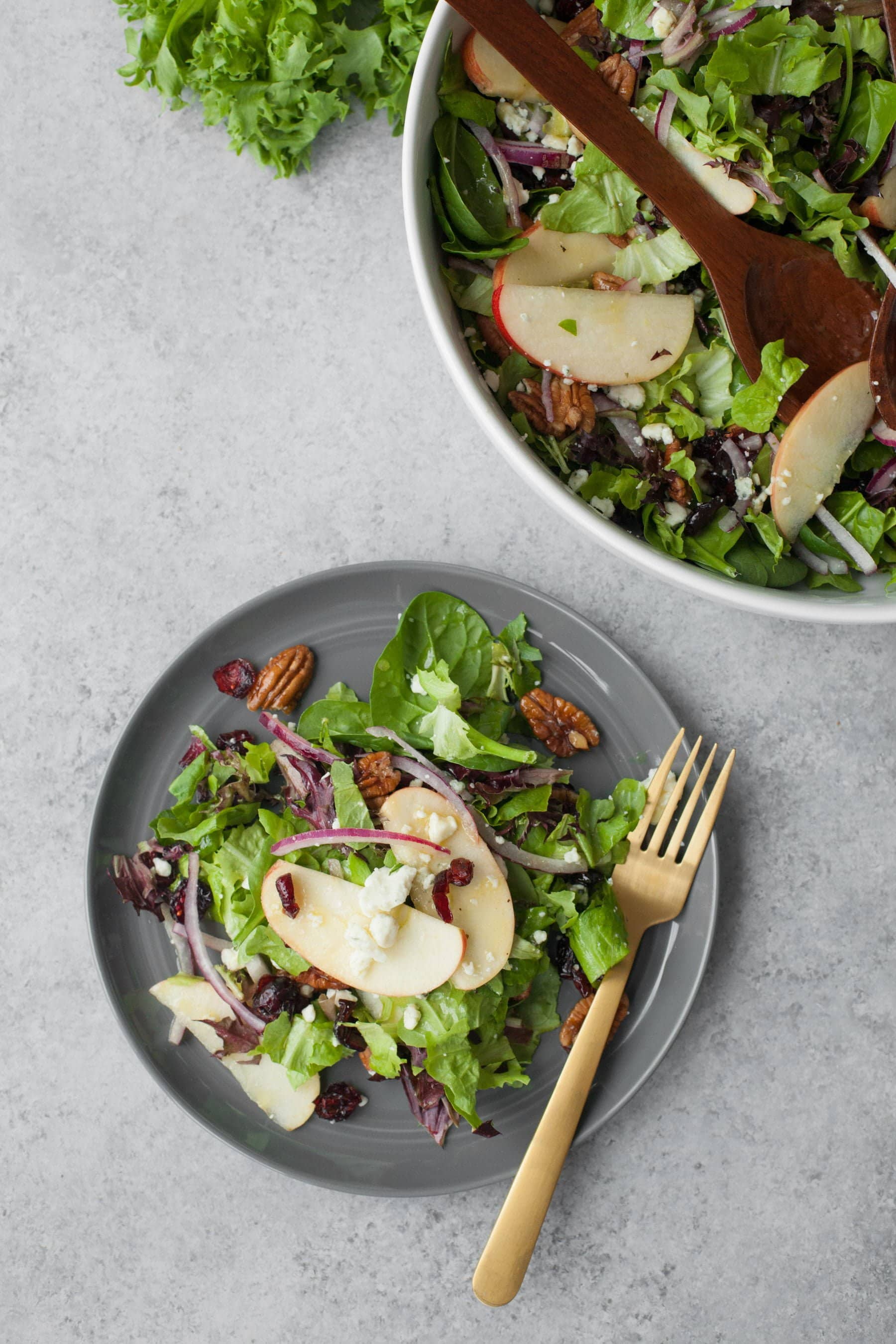 Close view of a plate piled high with salad alongside the serving bowl.