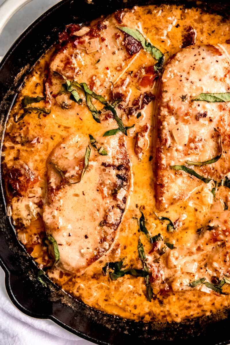 Tight view of cooked chicken breasts in a sun-dried tomato cream sauce garnished with chopped fresh basil.