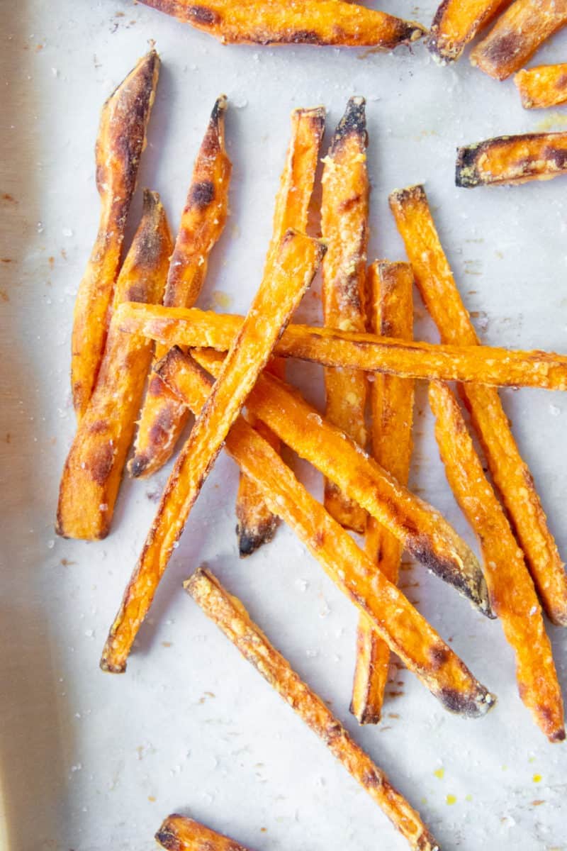 Sweet potato fries piled on top of each other on parchment paper.