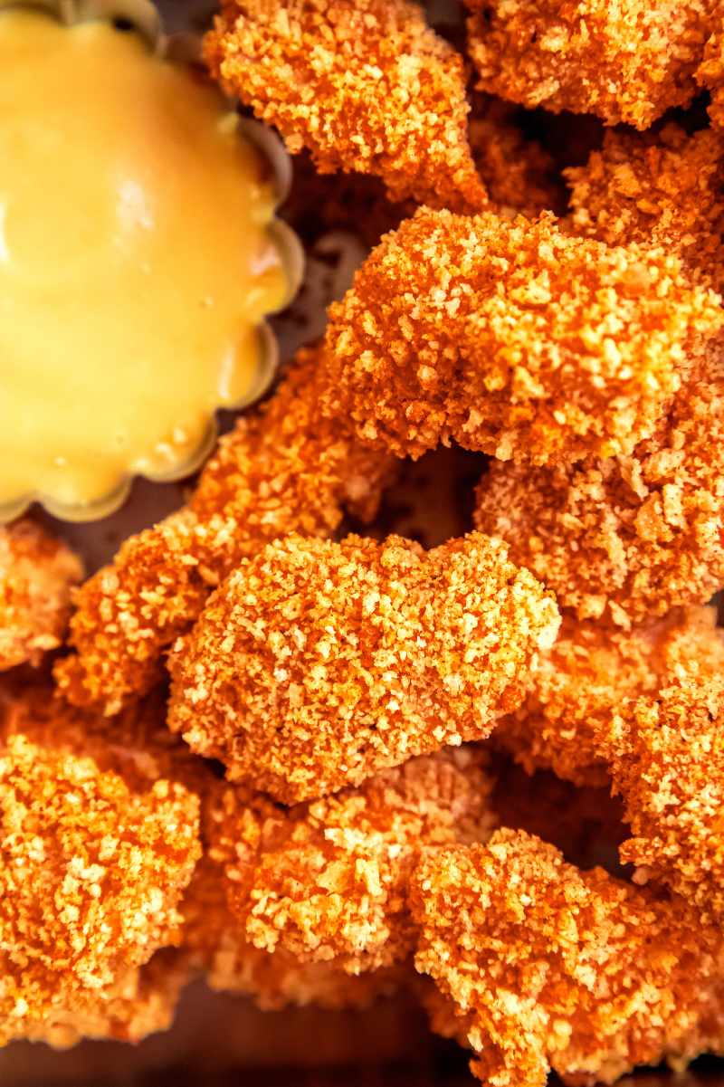 Tight view of crispy nuggets with a scalloped bowl of creamy dipping sauce .