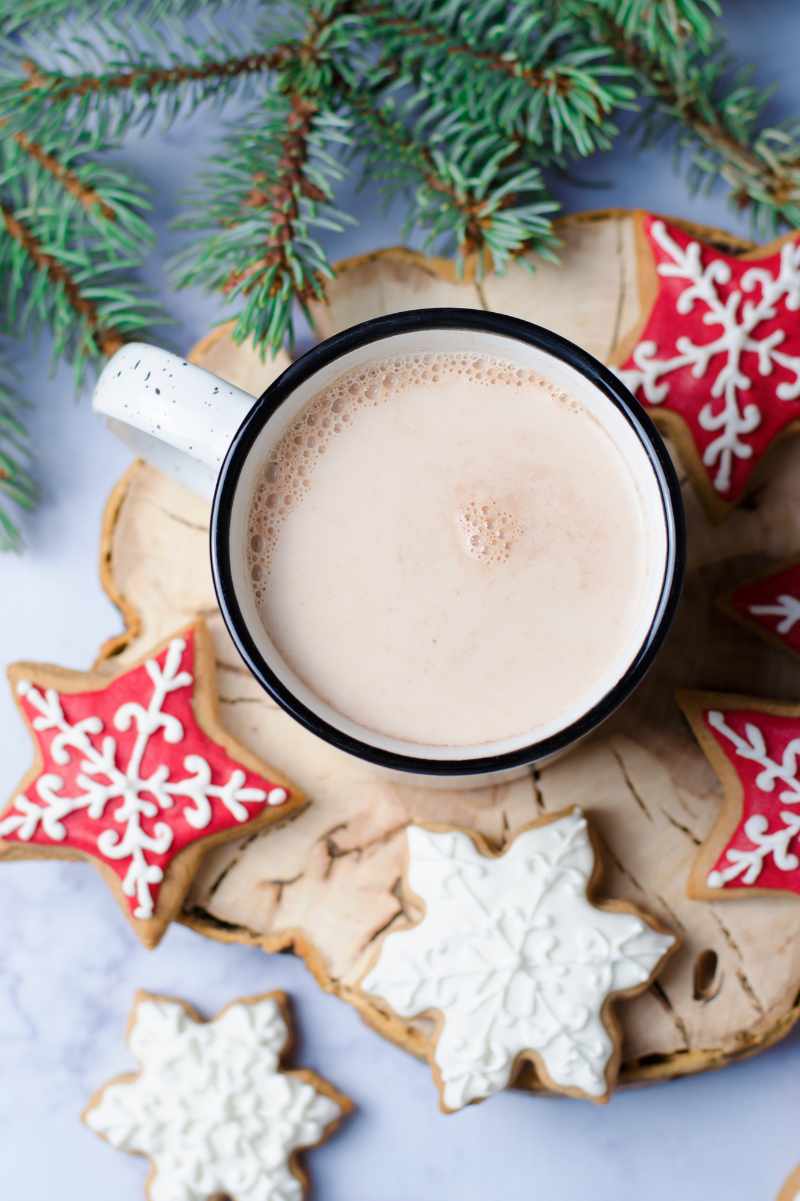 Overhead of a mug of crockpot hot chocolate, surrounded by star and snowflake-shaped cookies