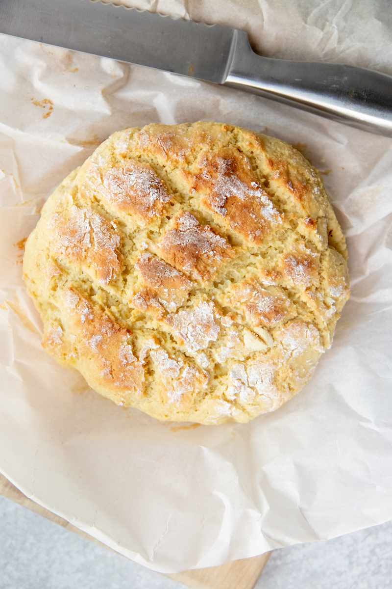 Overhead of a loaf of almond flour bread on parchment paper with a bread knife above it.