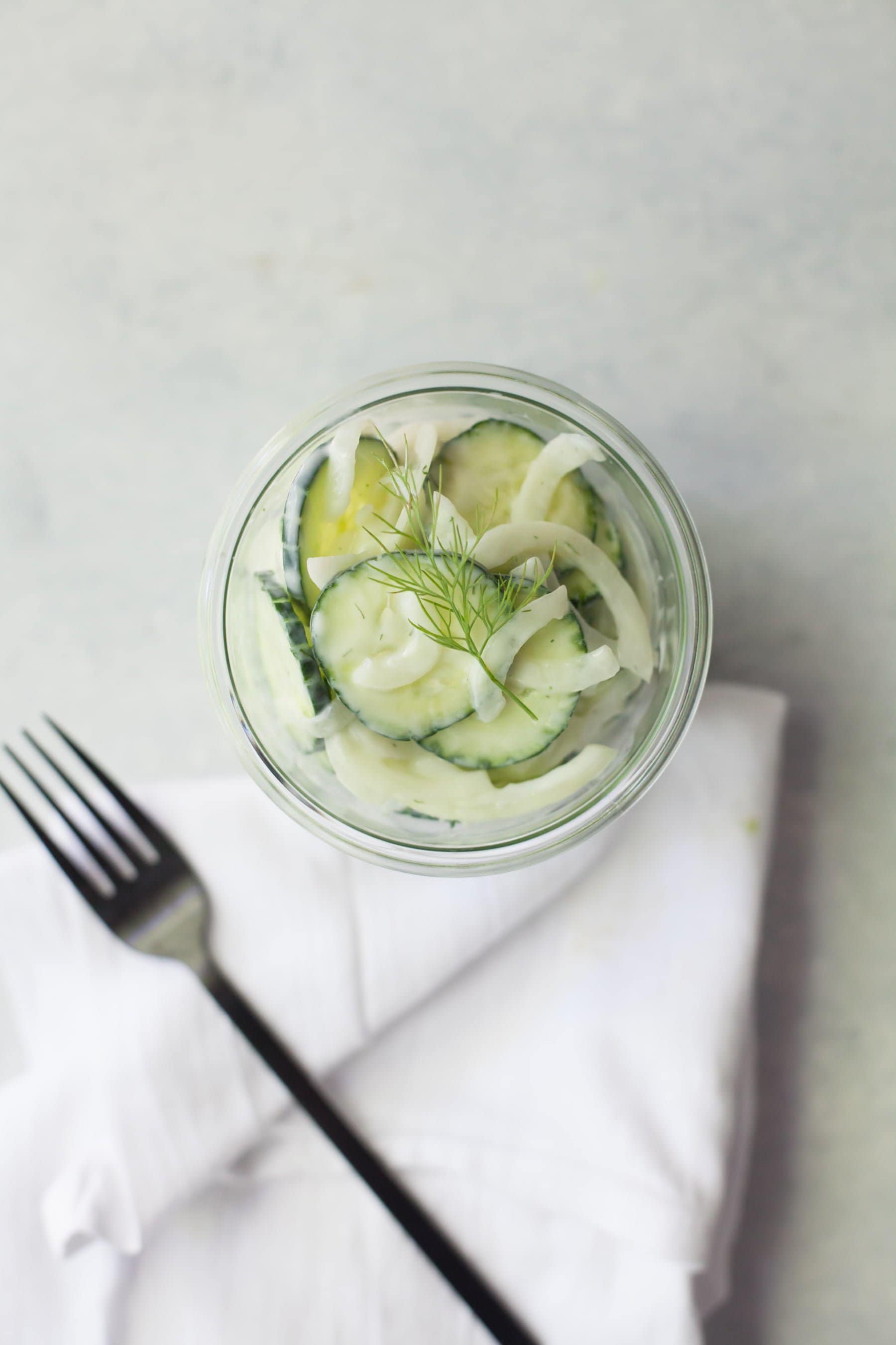 Overhead of finished salad in a jar with a linen napkin and fork nearby.