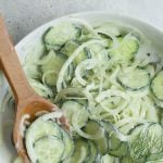 Overhead of dressed cucumber onion salad in a bow with a wooden spoon and fresh dill garnish. A text overlay reads, "Simple Cucumber and Onion Salad."