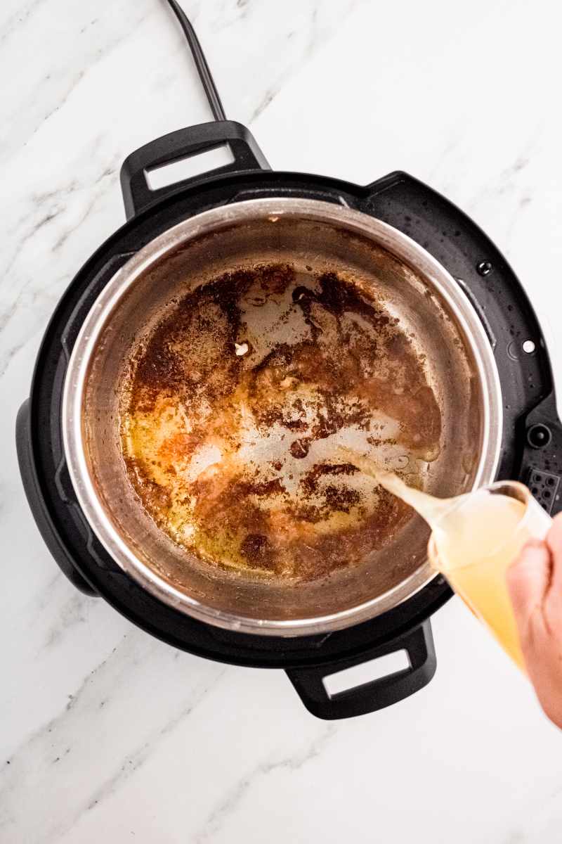 A hand pours chicken broth into the bottom of an instant pot to deglaze the pot.