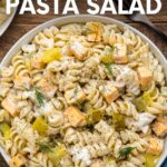 Top view of a bowl of dill pickle pasta salad on a wooden table with a blue kitchen linen and a fork. A text overlay reads, "Dill Pickle Pasta Salad."