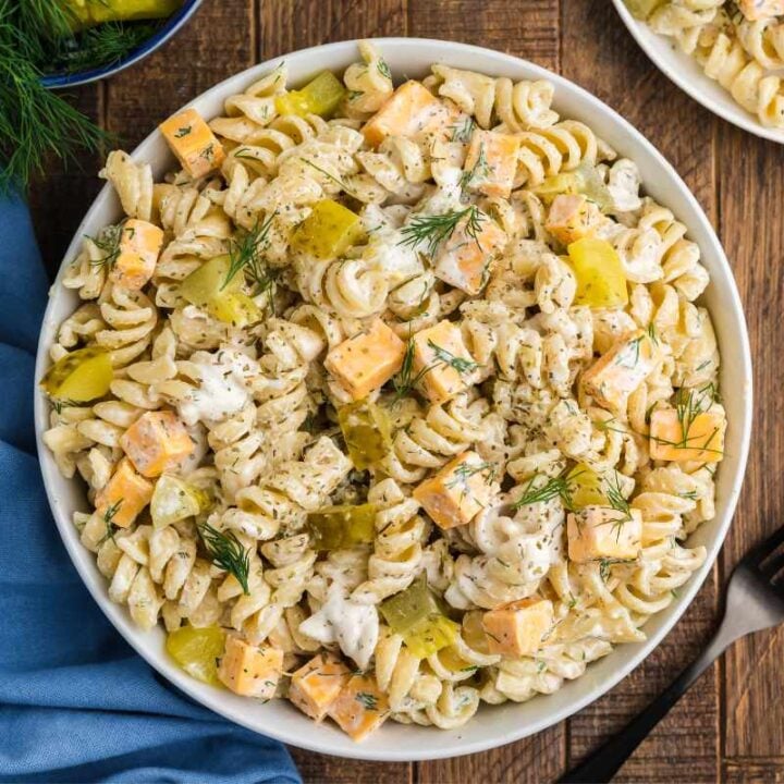 Top view of a bowl of dill pickle pasta salad on a wooden table with a blue kitchen linen and a fork.