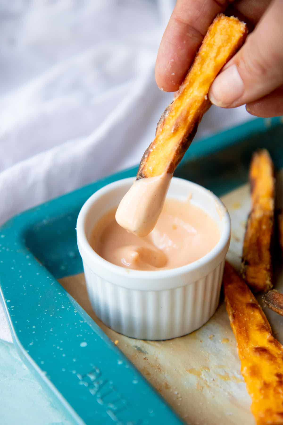 A hand dips a fry into a small ramekin of sauce