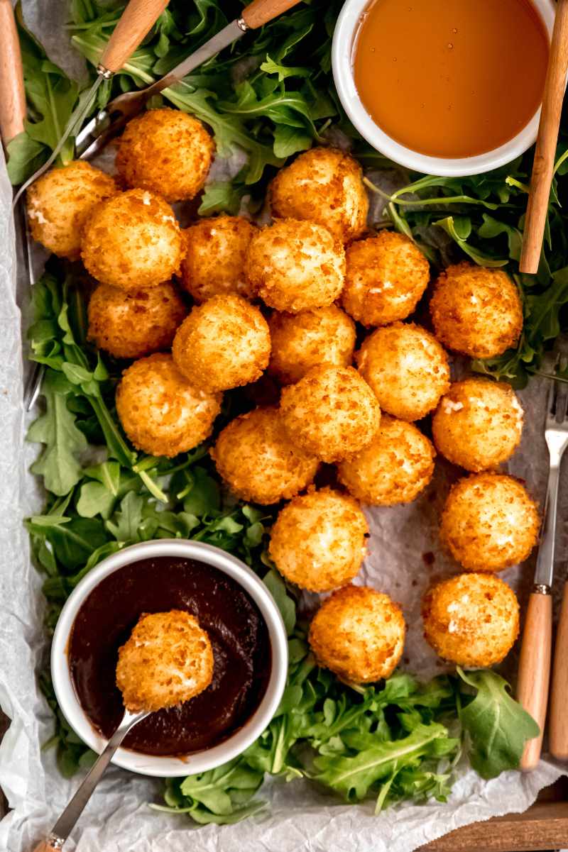 A long fondue-style fork dips a goat cheese ball into a small ramekin of jam.