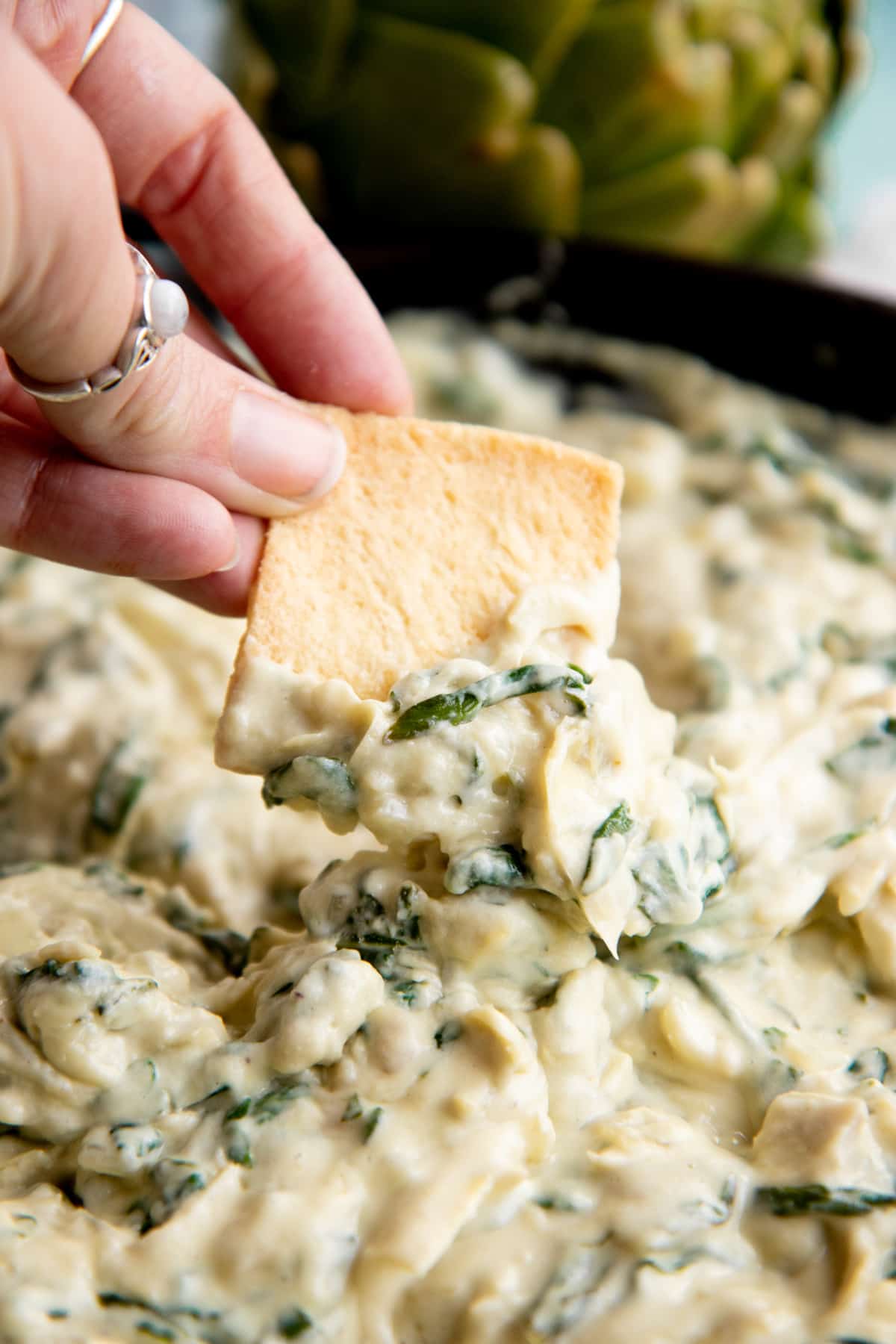 A hand dips a pita chip into a skillet of hot vegan spinach artichoke dip.