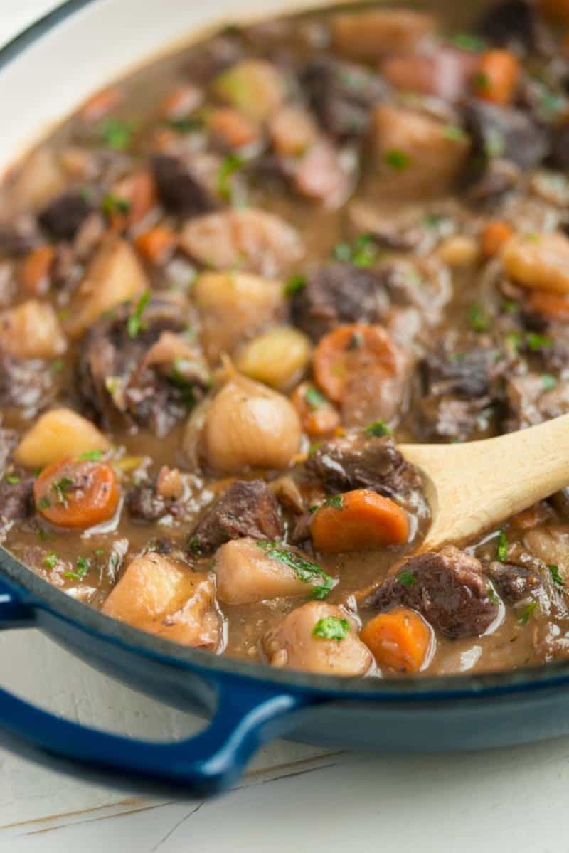 A wooden spoon scoops into a pot of beef stew with red wine