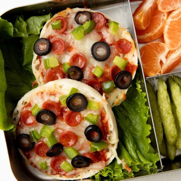 Close view of two English muffin pizzas in a three-compartment metal lunch box.