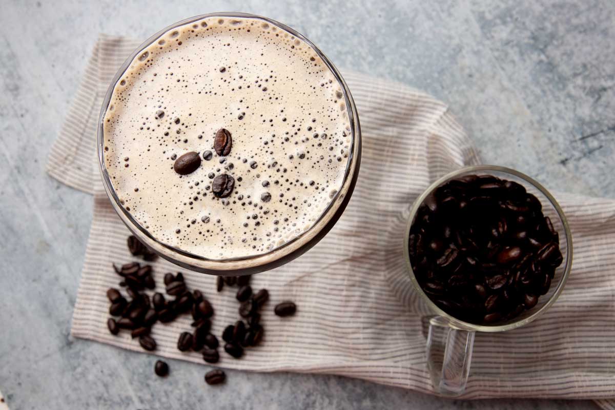 Top view of the creamy foam and espresso bean garnish on a classic espresso martini with additional beans alongside.