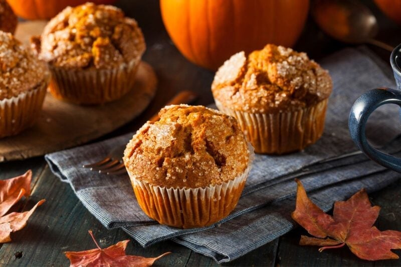 Two fall spiced muffins on a linen napkin served with a coffee mug nearby.