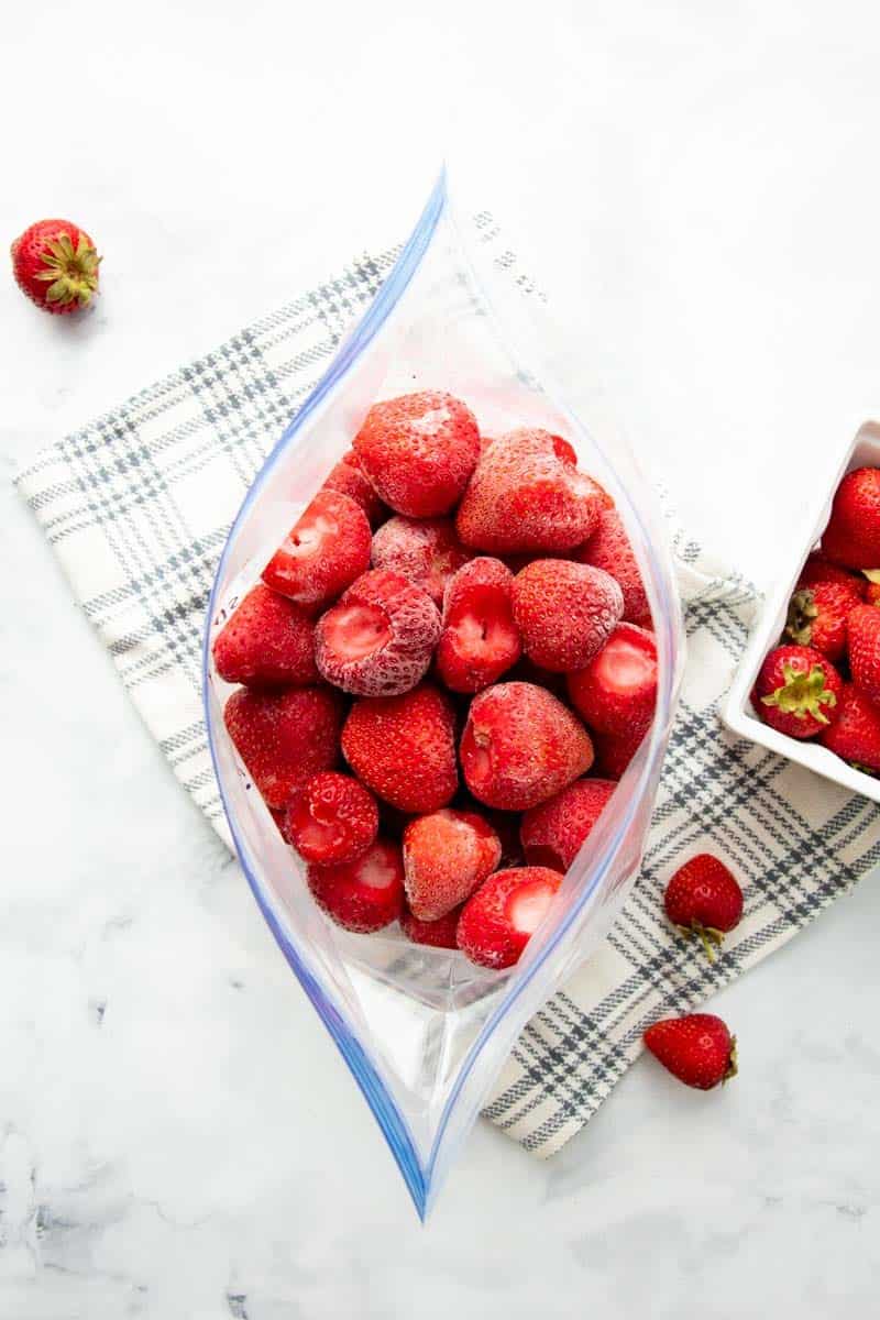 Overhead of plastic freezer bag open and filled with individually frozen whole strawberries.