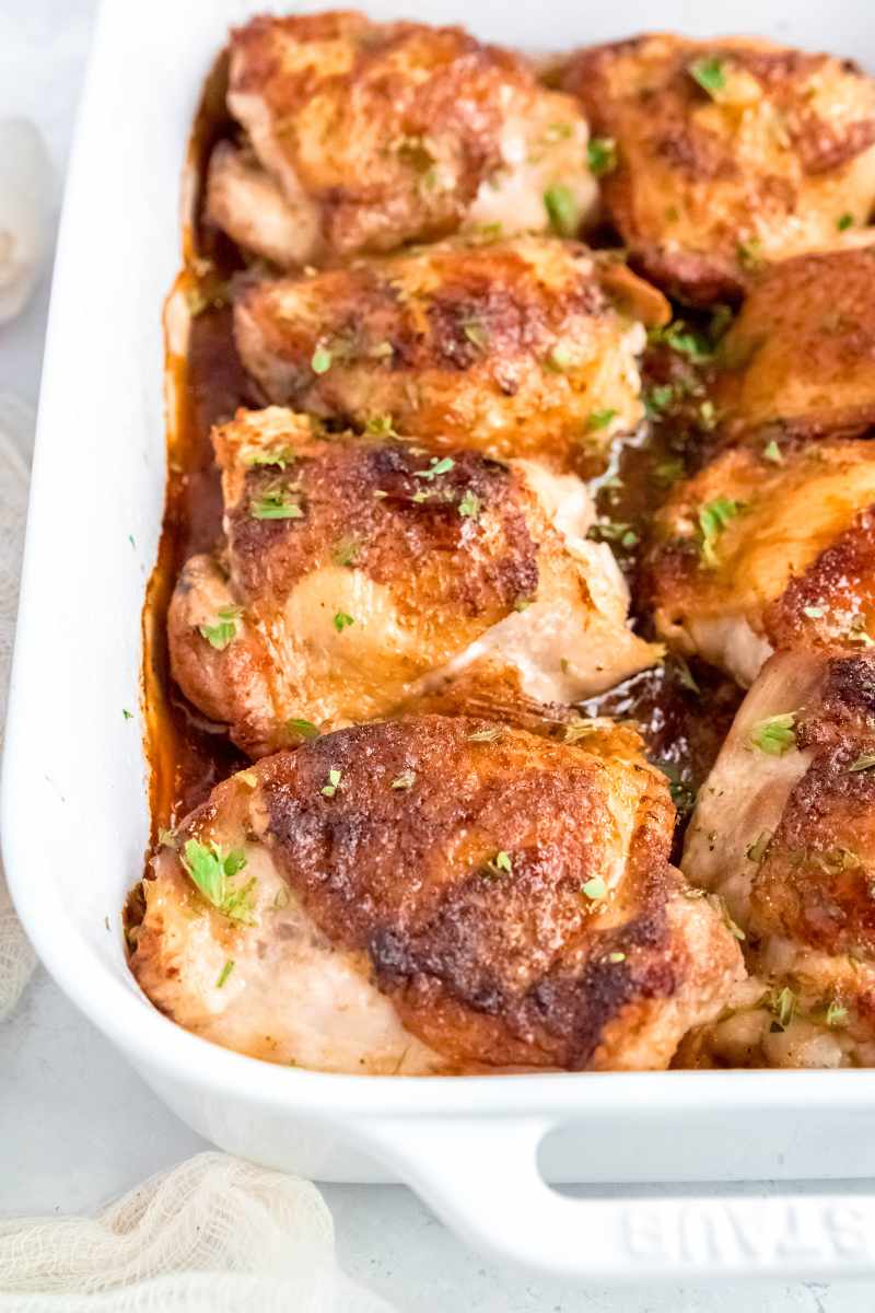 Close view of finished chicken thighs in a white casserole dish, topped with minced fresh herbs.