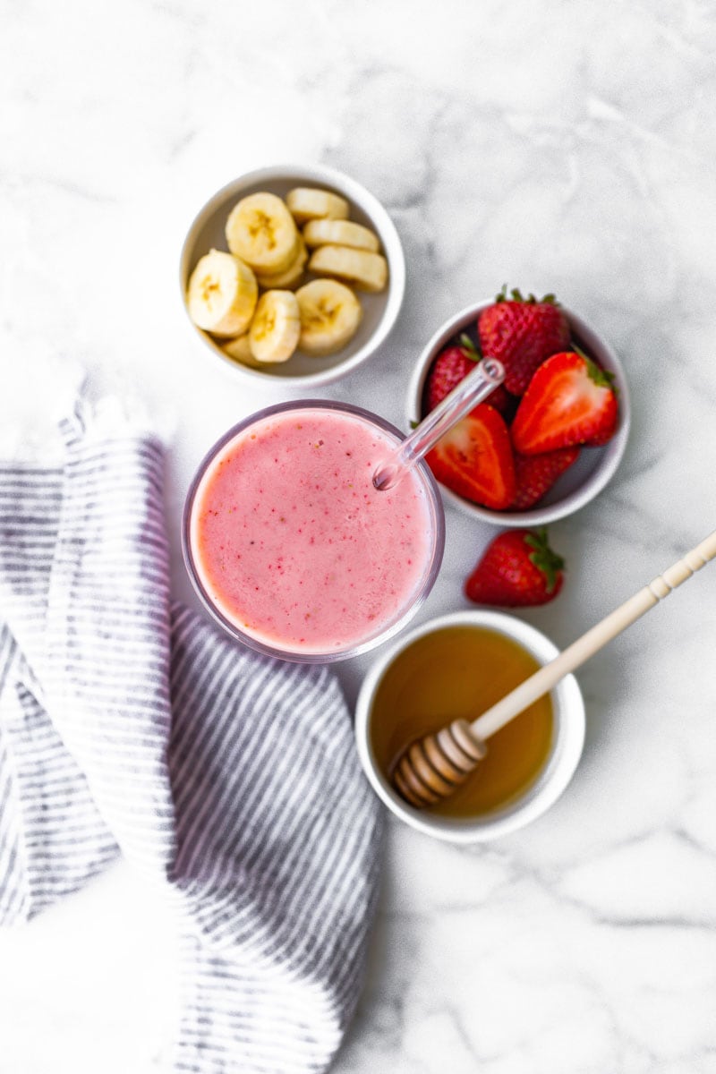 Overhead of pink smoothie with small bowls of fresh ingredients around it.