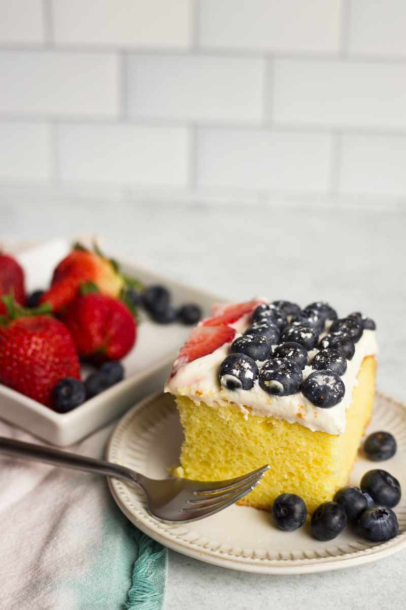 A tall slice of cake stands on a small plate with a fork and fresh berries around.