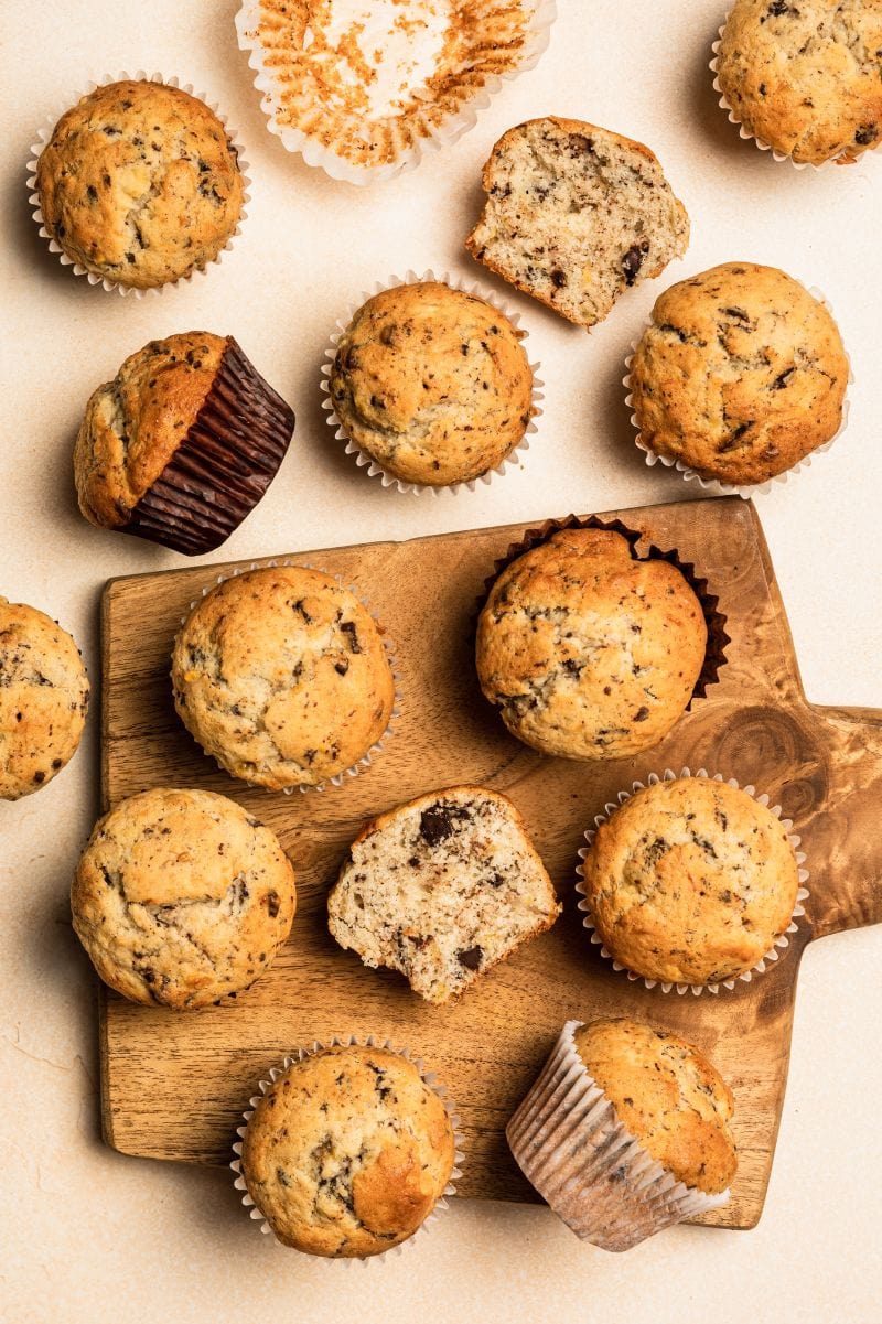 A dozen fluffy grain-free muffins on a light counter with a wooden serving board.