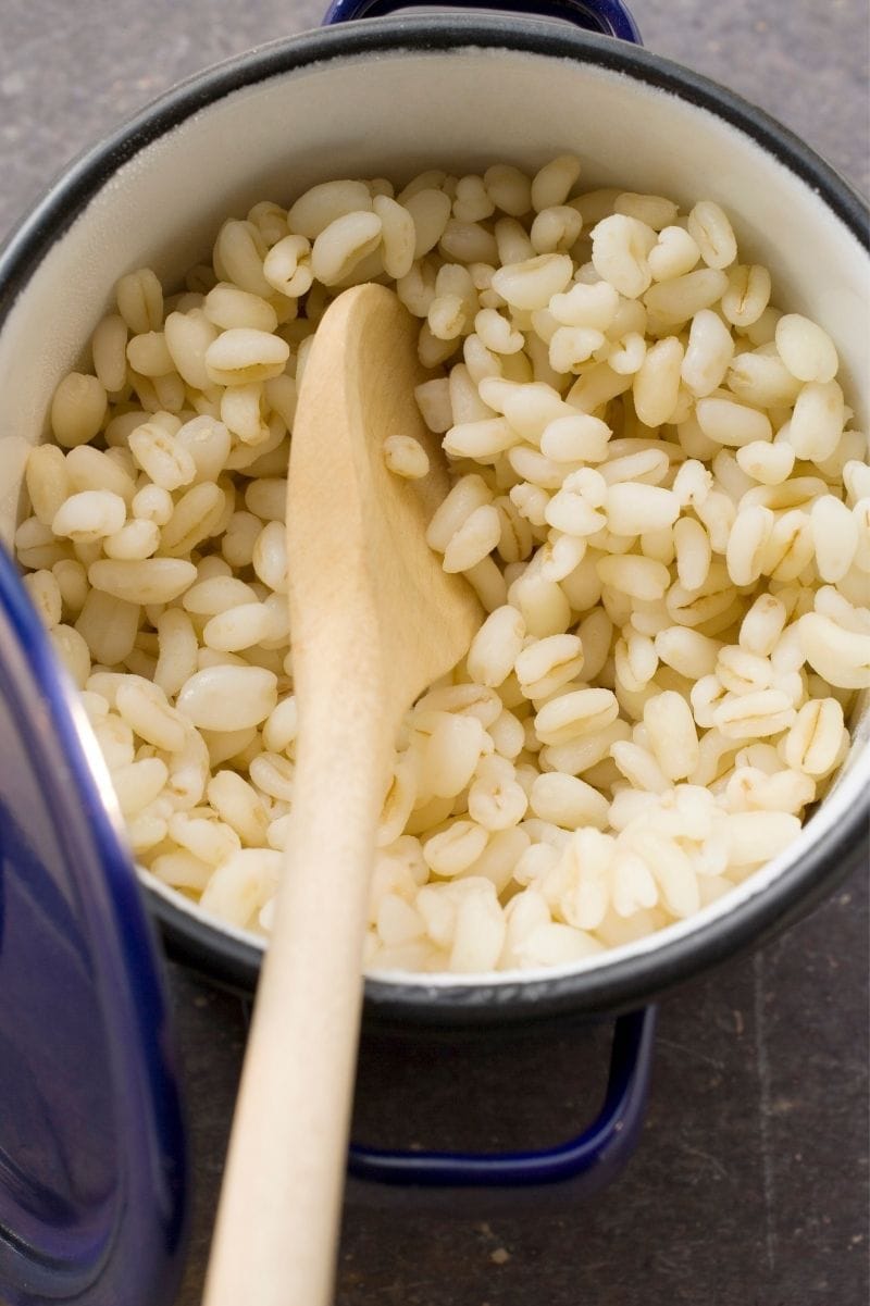 Fluffy cooked barley in a pot with a wooden spoon.