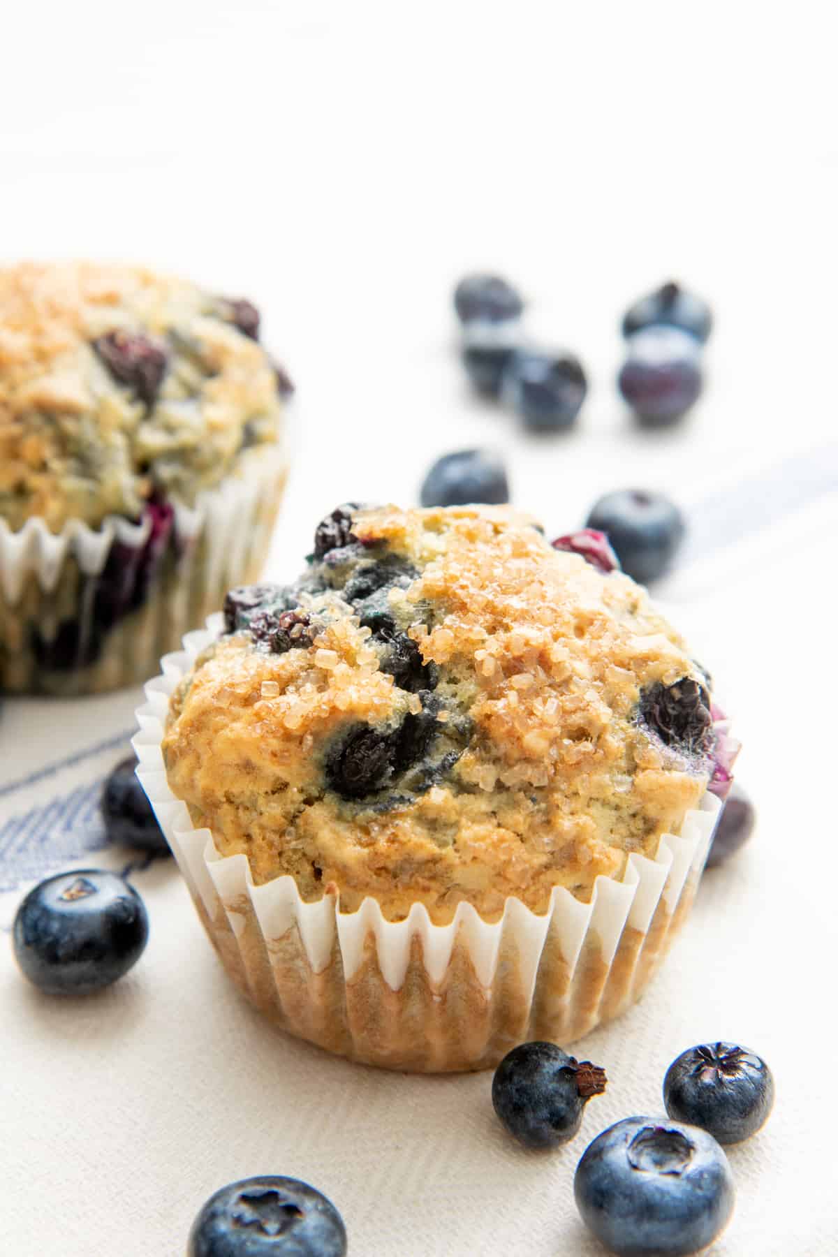 A baked Vegan Blueberry Muffin sits surrounded by fresh blueberries.