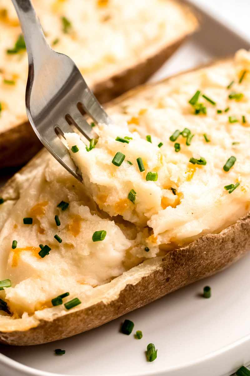 A fork digs into cheesy mashed potatoes stuffed into a baked potato shell.