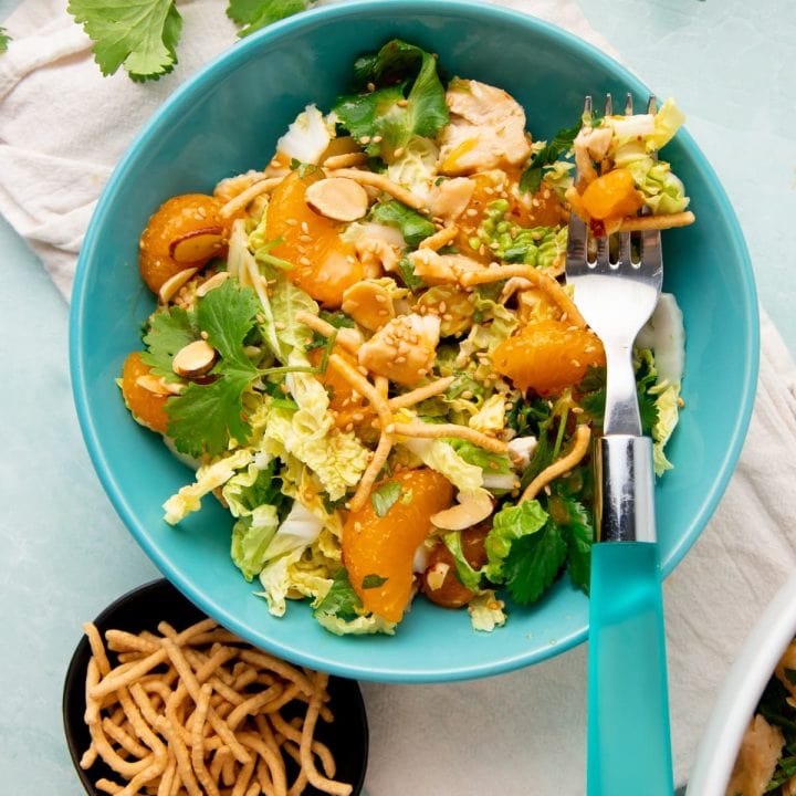 A forkful of mandarin chicken salad rests atop a single serving bowl of salad.