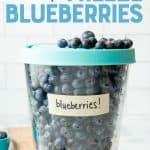 Close-up of tall glass freezer container with lid on, labeled and filled with individually frozen blueberries. A text overlay reads, "How to Freeze Blueberries."