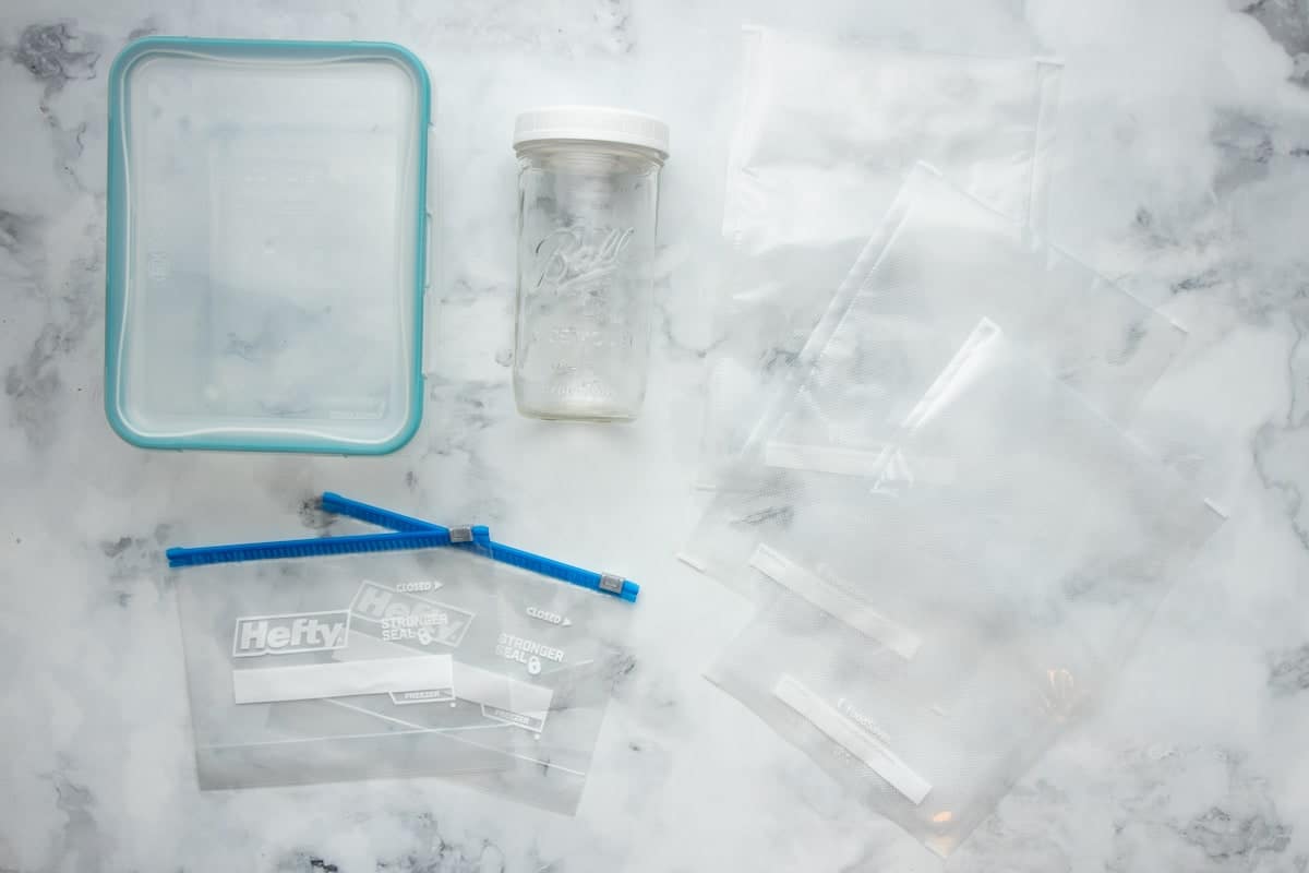 Overhead of various freezer containers such as vacuum seal bags, plastic zipper lock bags, glass containers with locking lids, and mason jars.