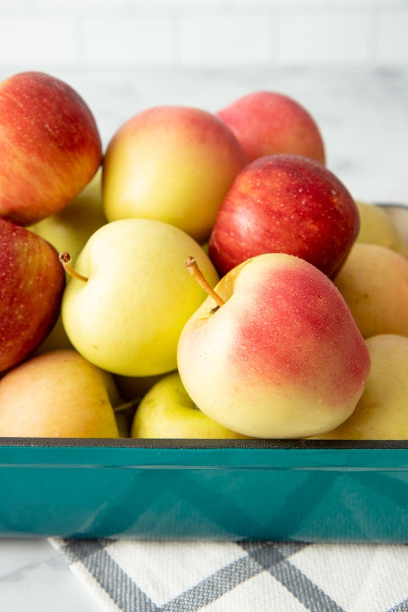 Fresh picked apples piled high in a baking dish sitting on a counter.