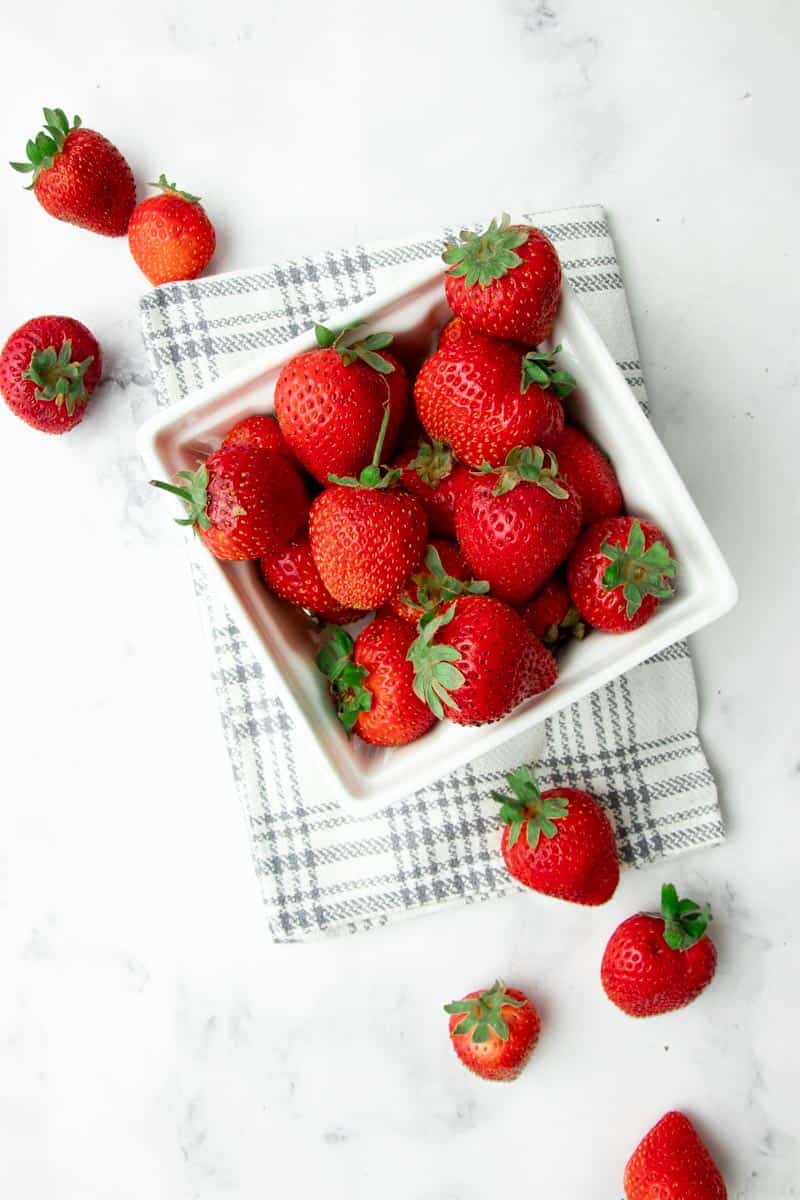 Overhead of fresh strawberries in a ceramic punnet with fresh berries spilling out.