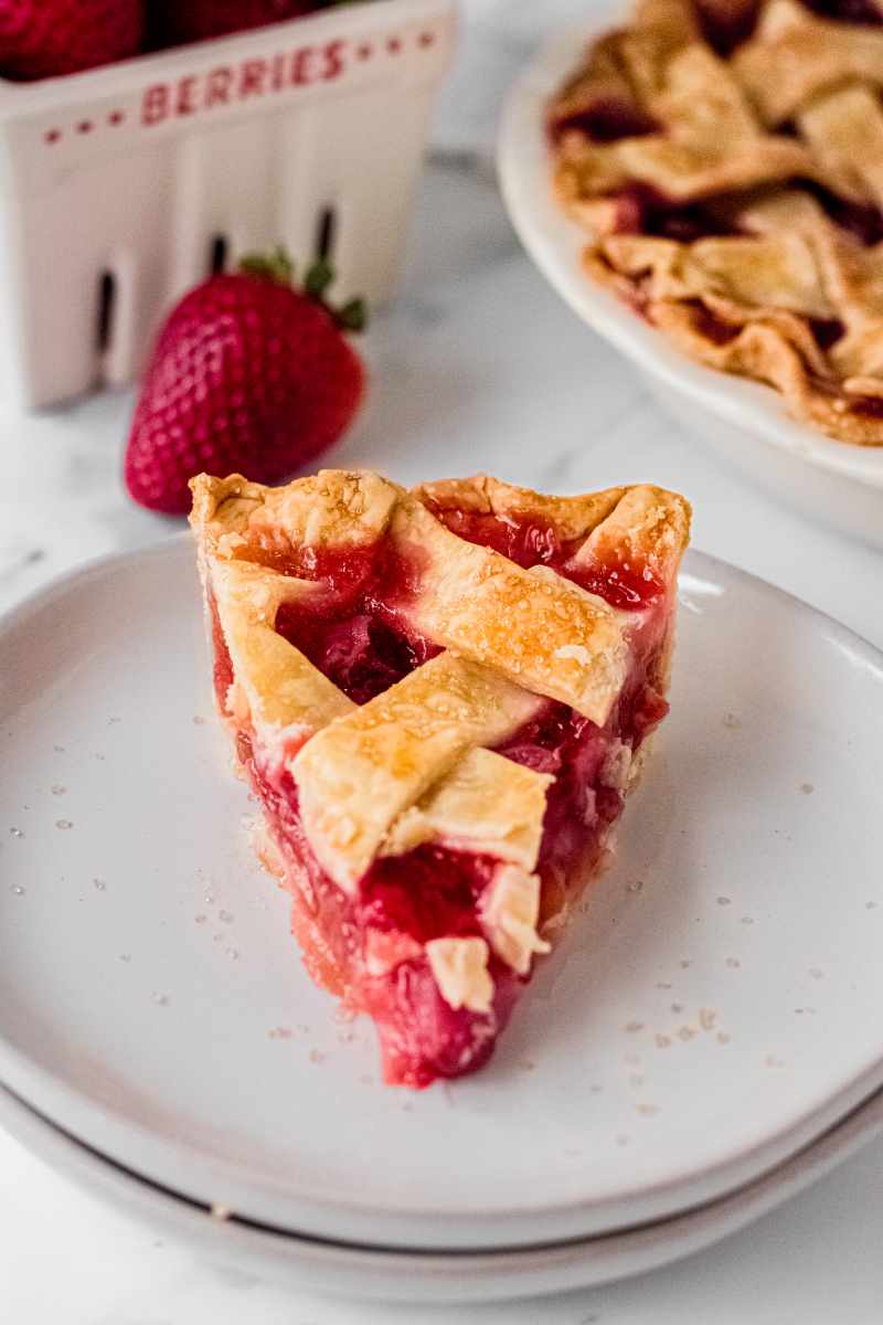 Front view of tall slice of strawberry rhubarb pie with a jammy red filling on a white plate.