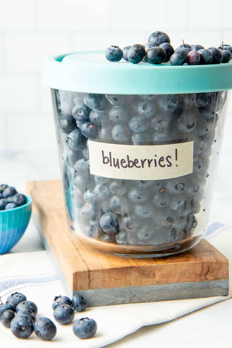 Close-up of tall glass freezer container with lid on, labeled and filled with individually frozen berries.