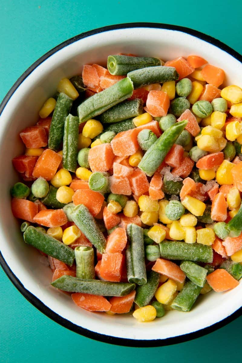 A bowl of frozen mixed vegetables sits on a teal background.