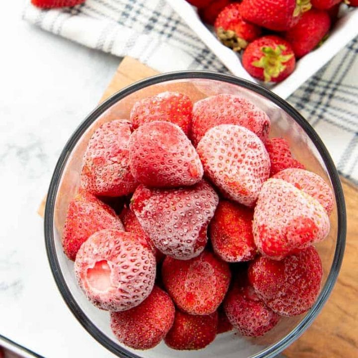 Overhead of whole, hulled, individually frozen strawberries in a glass container.