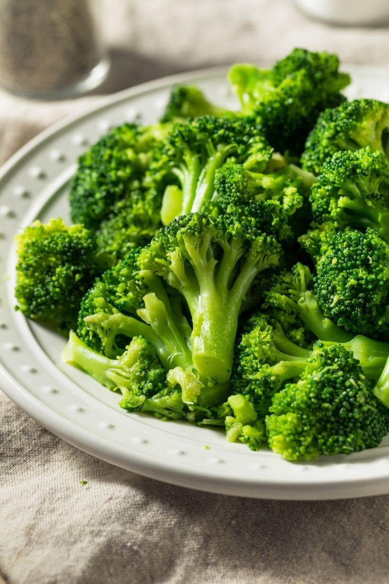 Steamed garlic broccoli served on a white plate with a linen tablecloth beneath.