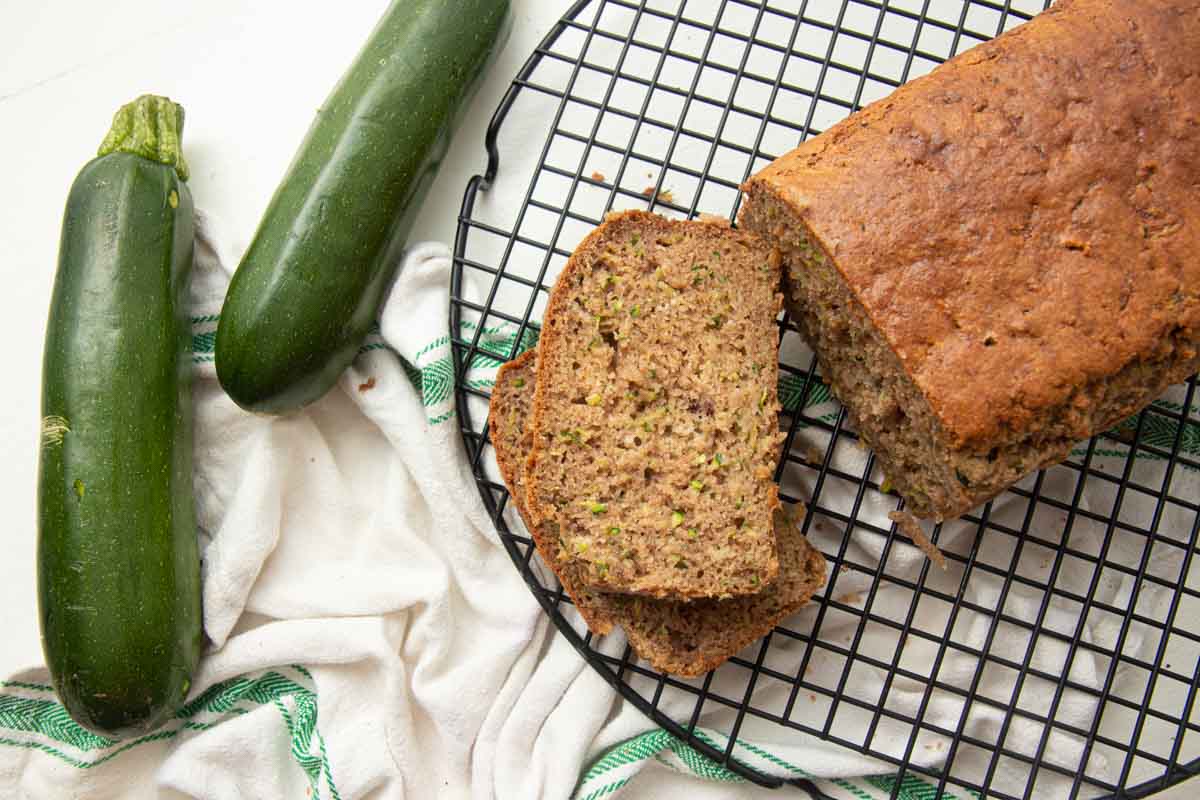 Overhead of a loaf of gluten-free zucchini bread on a cooling rack with two slices cut and stacked beside it.