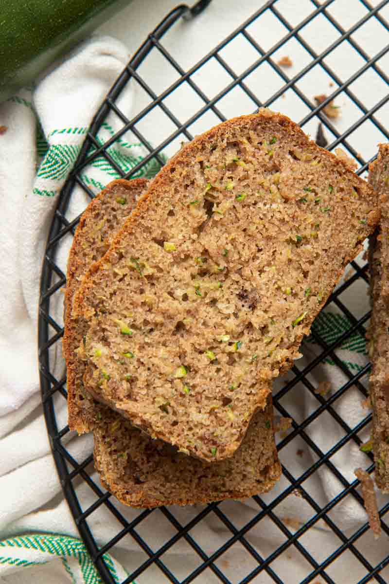 Close view of two slices of gluten-free zucchini bread stacked on a black cooling rack set over a kitchen towel.