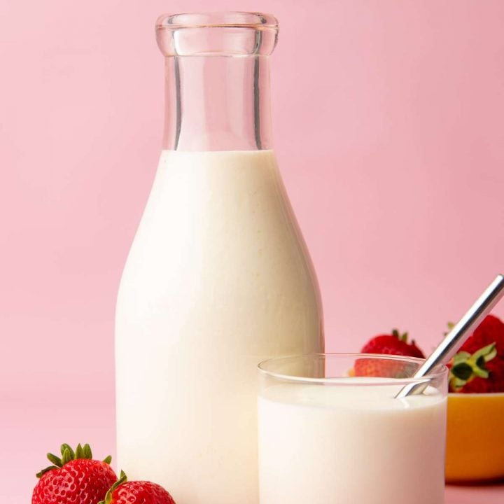 Close-up of a glass carafe and glass tumbler full of homemade kefir with ripe, red strawberries alongside.