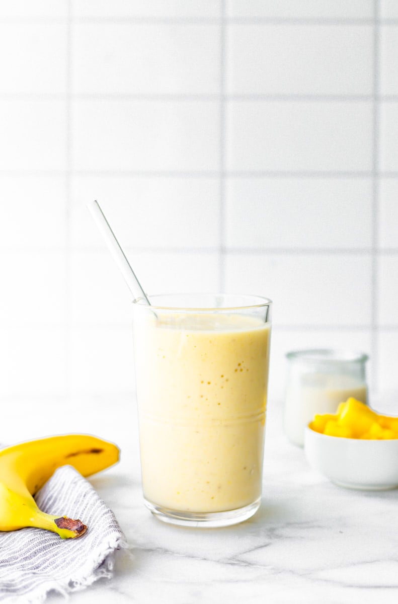 Pina colada smoothie on a counter with fresh banana and pineapple chunks.