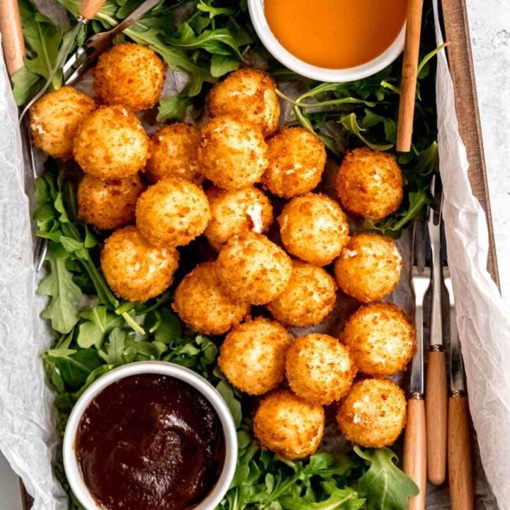 Overhead of an easy goat cheese appetizer platter served on a wooden tray with goat cheese balls, forks, honey, and jam.