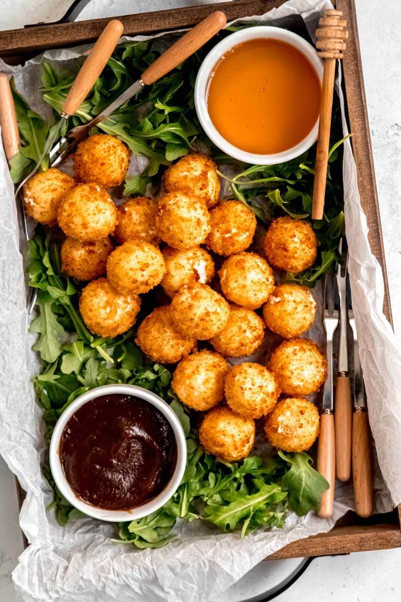 Overhead of an easy goat cheese appetizer platter served on a wooden tray with goat cheese balls, forks, honey, and jam.