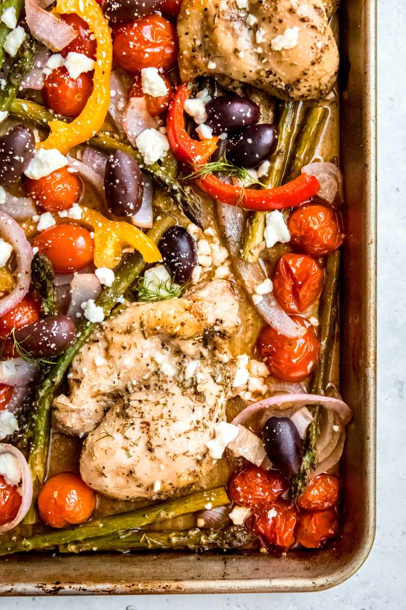 Overhead of the corner of a baking pan filled with chicken and veggies topped with feta and herbs.