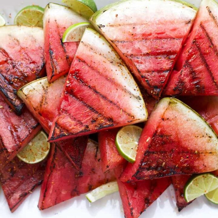 Lime slices are tucked around grilled watermelon slices on a white serving dish.