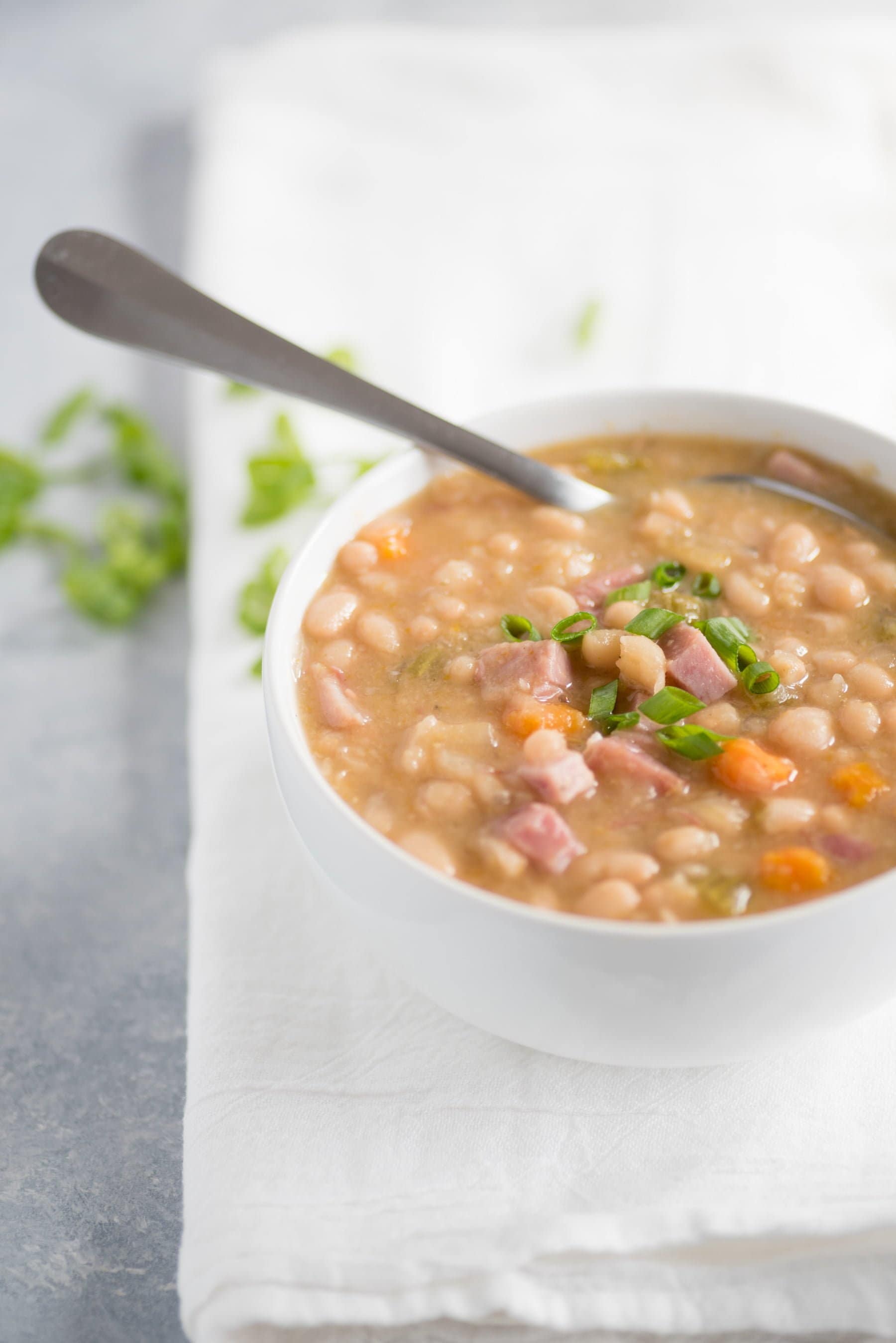 A white bowl filled with ham and beans sits on a folded white cloth.